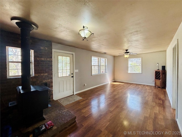 foyer entrance with baseboards, a wood stove, wood finished floors, a textured ceiling, and a ceiling fan