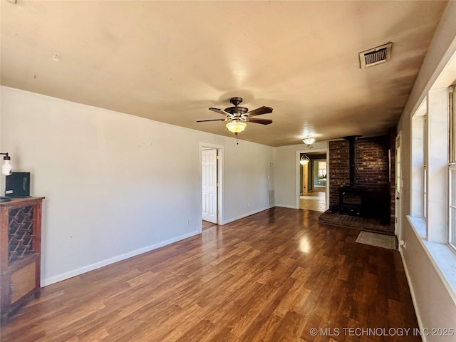 unfurnished living room featuring visible vents, a ceiling fan, wood finished floors, baseboards, and a wood stove