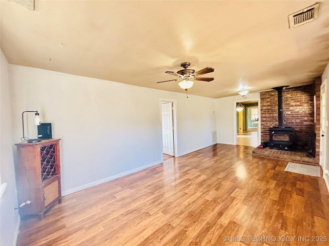 unfurnished living room featuring a ceiling fan, visible vents, baseboards, a wood stove, and light wood-style floors