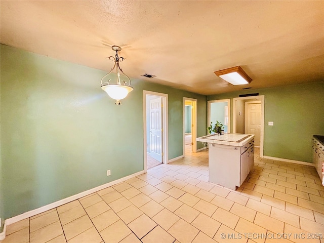 kitchen with visible vents, pendant lighting, a kitchen island, light tile patterned floors, and tile counters