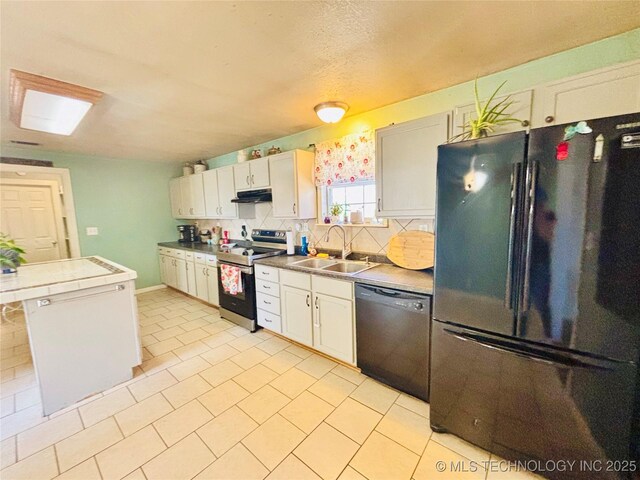 kitchen with under cabinet range hood, tile countertops, decorative backsplash, black appliances, and a sink