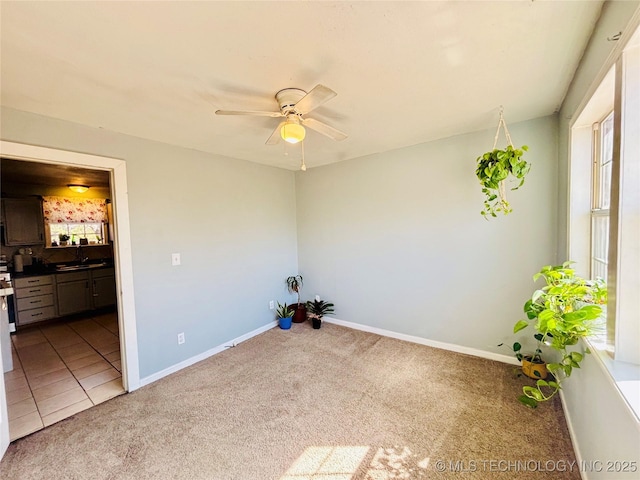 carpeted spare room featuring tile patterned flooring, ceiling fan, baseboards, and a sink