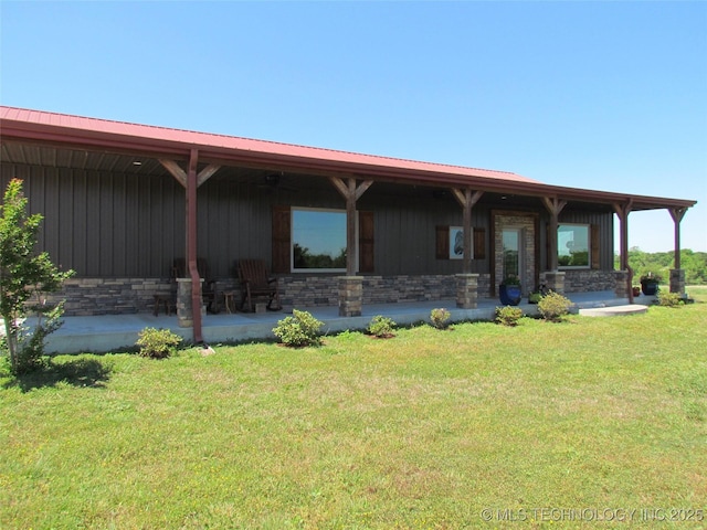 back of house with metal roof, stone siding, and a lawn