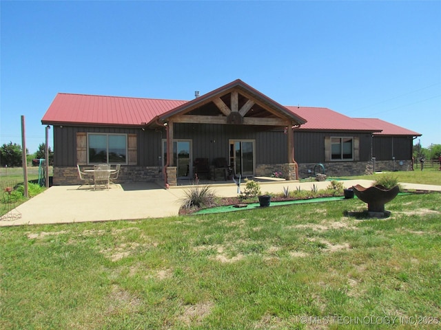 rear view of property featuring board and batten siding, a patio, a yard, and stone siding