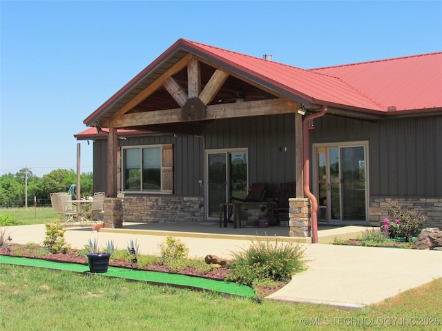 rear view of house with metal roof, stone siding, board and batten siding, and a patio