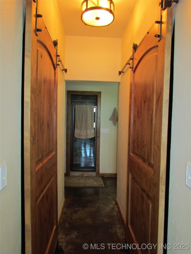 hall featuring a barn door, baseboards, and concrete floors