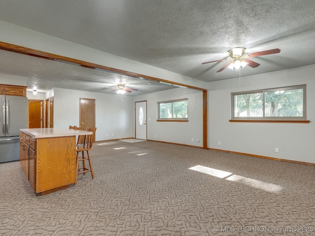 kitchen with brown cabinetry, freestanding refrigerator, light countertops, a kitchen bar, and light colored carpet