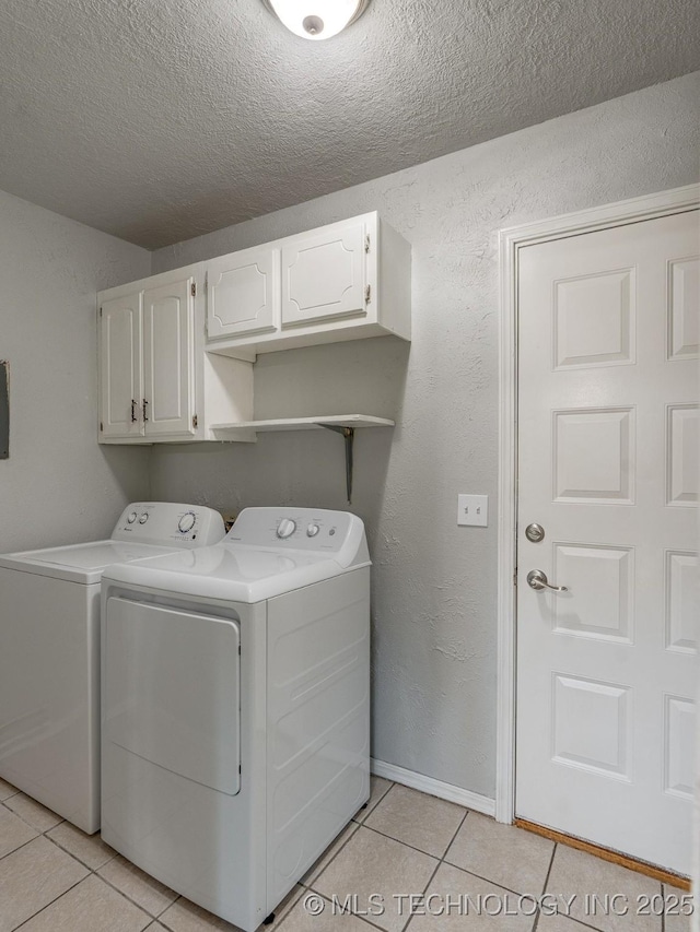 clothes washing area featuring a textured ceiling, washing machine and dryer, cabinet space, light tile patterned floors, and a textured wall