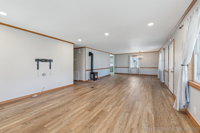 empty room with visible vents, a notable chandelier, light wood-style floors, crown molding, and a wood stove