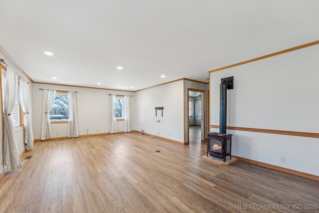 empty room with light wood finished floors, baseboards, ornamental molding, recessed lighting, and a wood stove