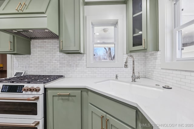 kitchen with green cabinets, white gas stove, under cabinet range hood, light countertops, and a sink