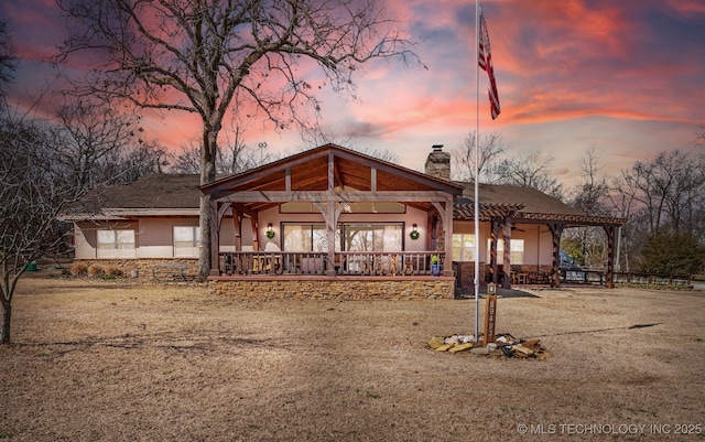 back of property at dusk with stucco siding, stone siding, a chimney, and a pergola