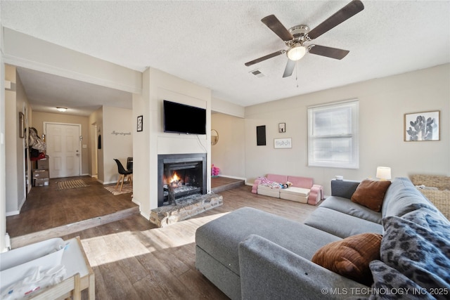 living area featuring visible vents, ceiling fan, a lit fireplace, wood finished floors, and a textured ceiling