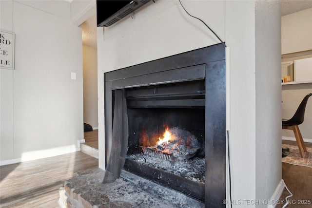 details with baseboards, a warm lit fireplace, and wood finished floors