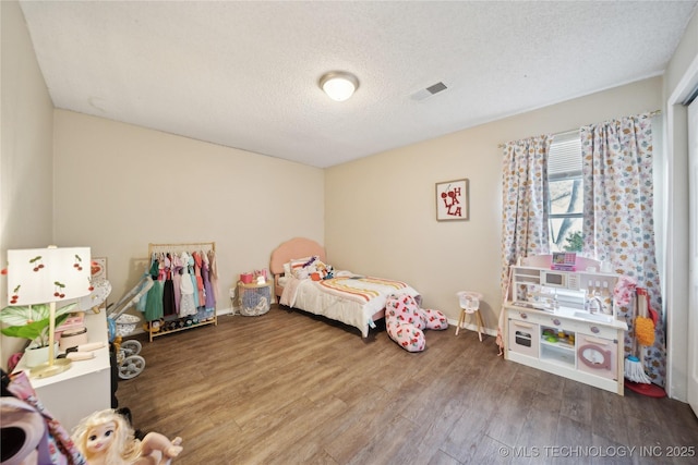 bedroom with baseboards, wood finished floors, visible vents, and a textured ceiling