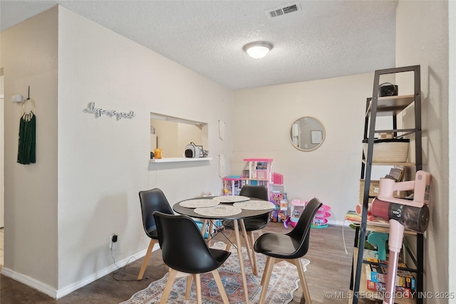 dining room with visible vents, baseboards, a textured ceiling, and wood finished floors