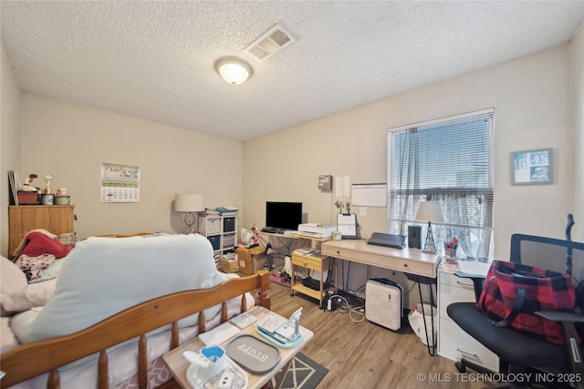 bedroom with visible vents, a textured ceiling, and wood finished floors