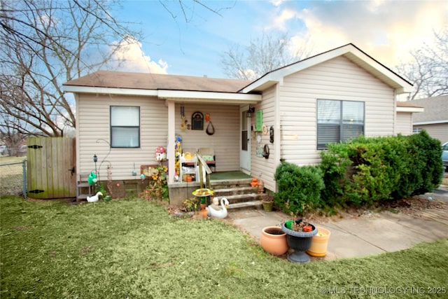 view of front of house with covered porch, a front yard, and fence