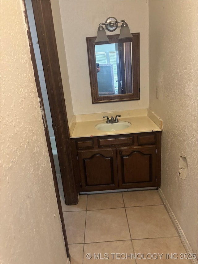 bathroom with tile patterned flooring, vanity, baseboards, and a textured wall