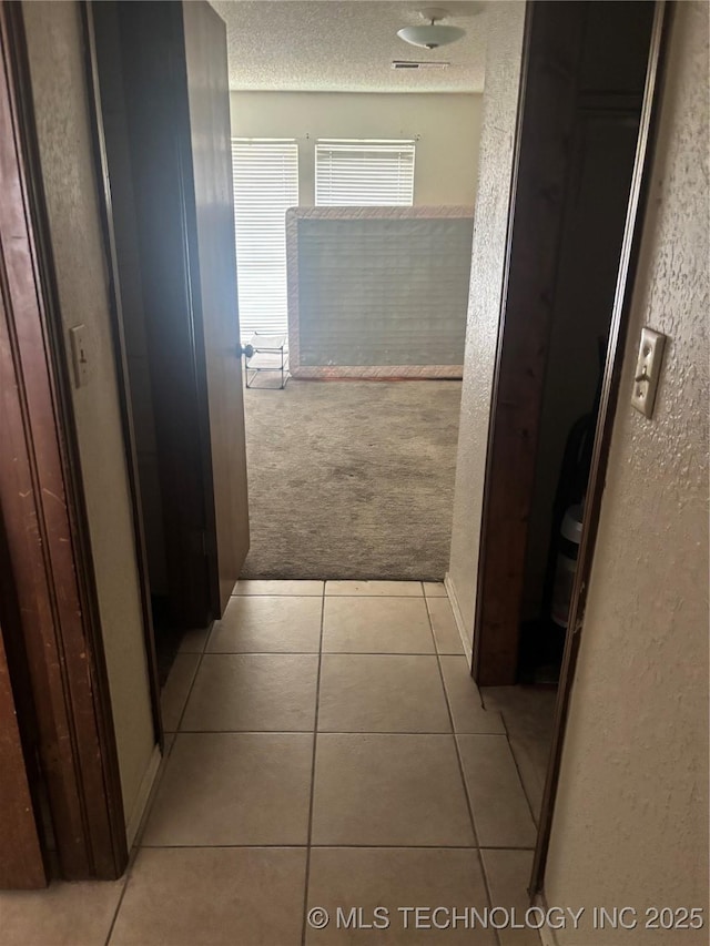 corridor with light tile patterned floors, light colored carpet, a textured ceiling, and a textured wall