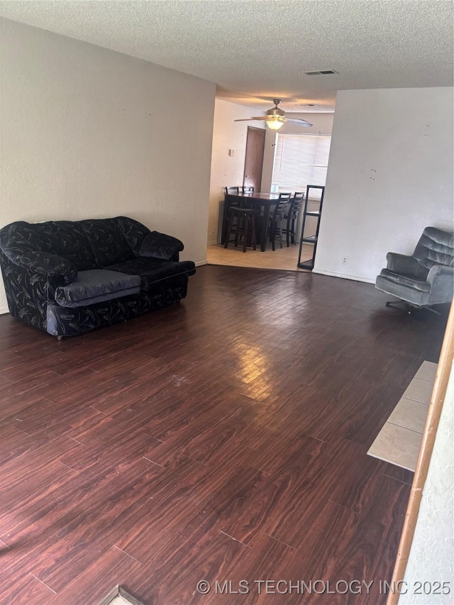 living room featuring ceiling fan, visible vents, a textured ceiling, and wood finished floors