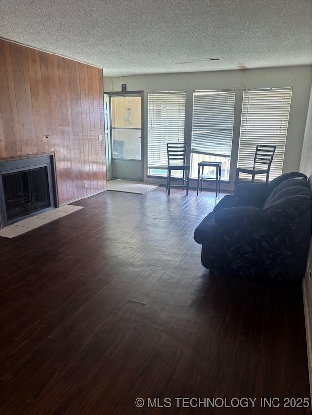 unfurnished living room with a fireplace with flush hearth, wood walls, a textured ceiling, and wood finished floors