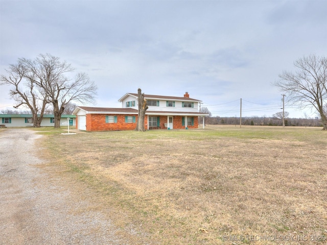 view of front facade with a front yard, driveway, an attached garage, a chimney, and brick siding