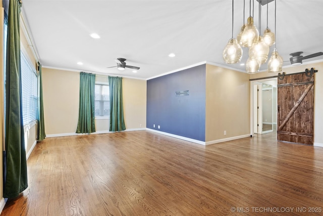 spare room with a barn door, crown molding, wood finished floors, and a ceiling fan