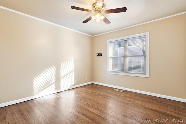 empty room featuring crown molding, wood finished floors, baseboards, and visible vents