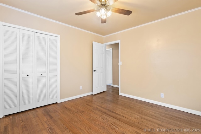 unfurnished bedroom featuring ornamental molding, a ceiling fan, wood finished floors, a closet, and baseboards