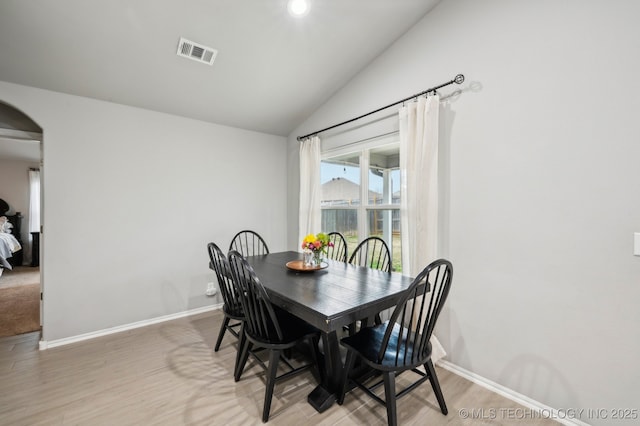 dining room with visible vents, arched walkways, baseboards, and vaulted ceiling