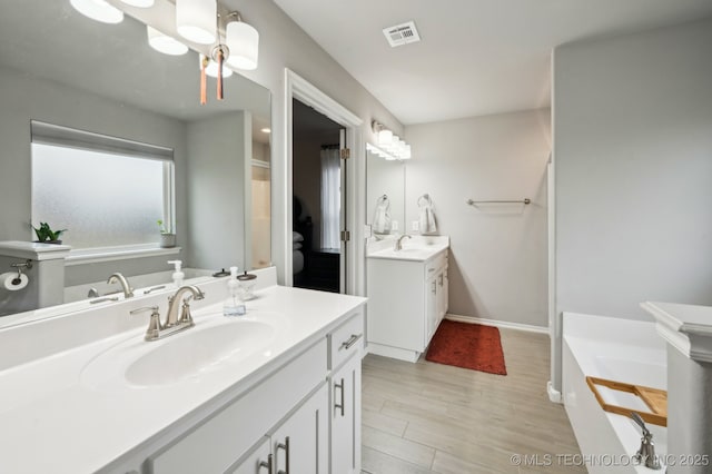 bathroom with a sink, visible vents, a tub to relax in, and two vanities