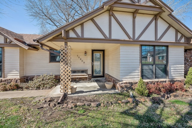 doorway to property featuring stucco siding, covered porch, and a shingled roof