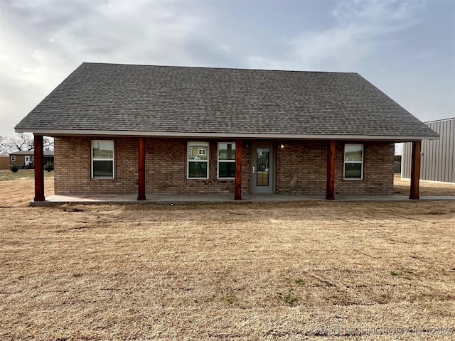 rear view of house featuring a yard, a patio area, brick siding, and roof with shingles