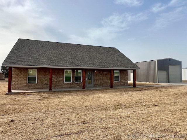 view of front of property featuring an outbuilding, brick siding, a detached garage, and a shingled roof