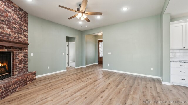 unfurnished living room with baseboards, a fireplace, light wood-style floors, and ceiling fan