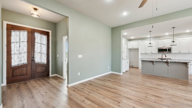 interior space featuring stainless steel microwave, backsplash, light wood-style flooring, french doors, and white cabinets