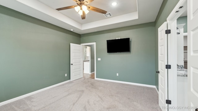 unfurnished bedroom with visible vents, ceiling fan, baseboards, a tray ceiling, and carpet floors
