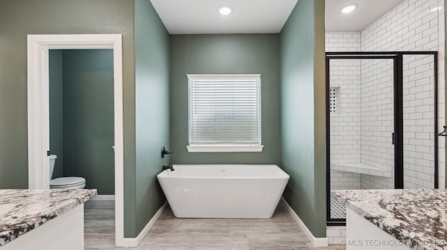 full bathroom featuring a shower stall, a freestanding bath, toilet, wood finished floors, and vanity