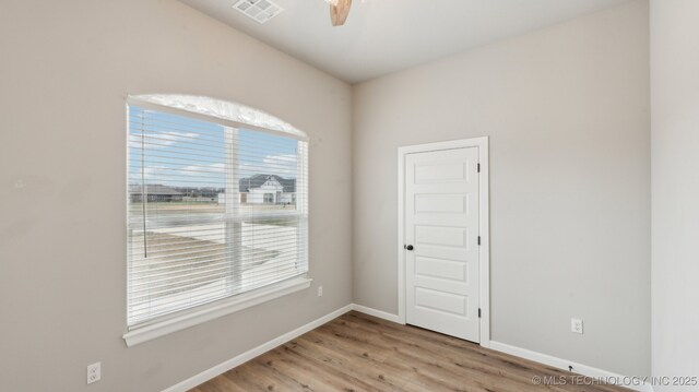 unfurnished room featuring wood finished floors, visible vents, a wealth of natural light, and baseboards