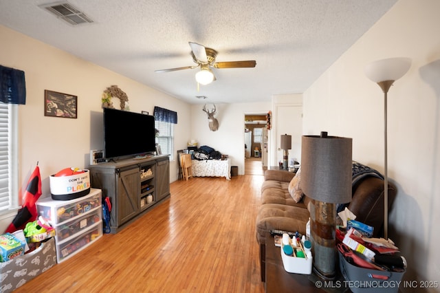 living area featuring visible vents, a textured ceiling, a ceiling fan, and light wood finished floors