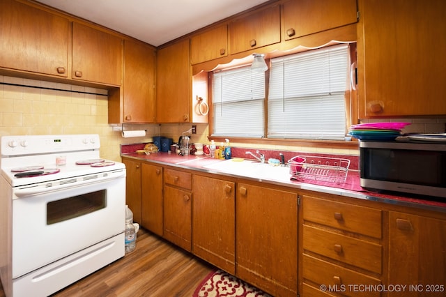 kitchen featuring brown cabinetry, a sink, stainless steel microwave, white electric range, and light wood-type flooring