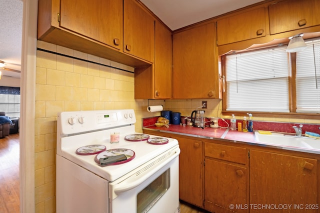 kitchen featuring a sink, electric range, plenty of natural light, and brown cabinetry