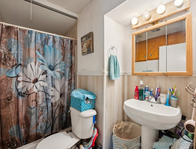 bathroom with a wainscoted wall, toilet, a shower with shower curtain, and visible vents