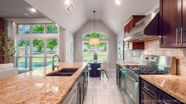 kitchen featuring stainless steel range with gas cooktop, a sink, wall chimney range hood, lofted ceiling, and light stone counters