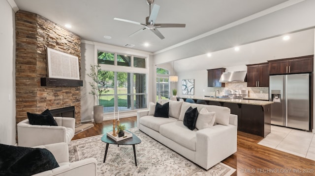 living area featuring ceiling fan, ornamental molding, light wood-type flooring, a stone fireplace, and recessed lighting