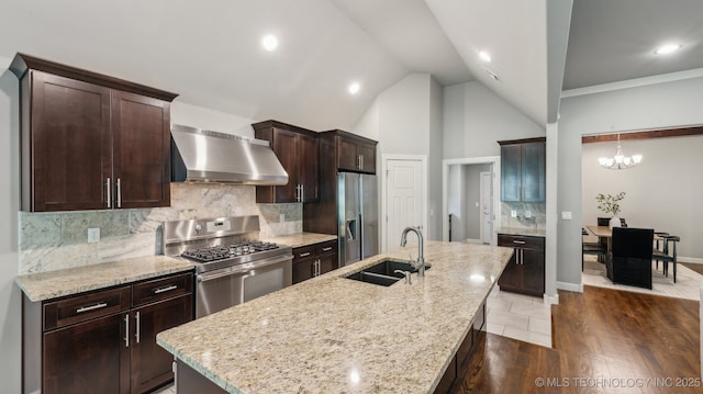 kitchen with wall chimney range hood, appliances with stainless steel finishes, a sink, dark brown cabinets, and light stone counters