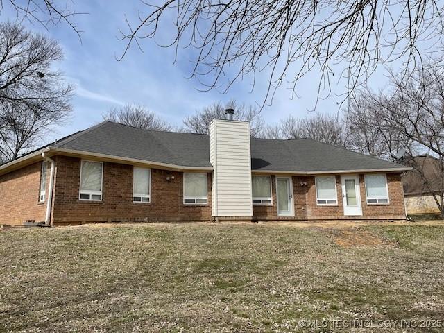 rear view of property featuring brick siding, a chimney, and a yard