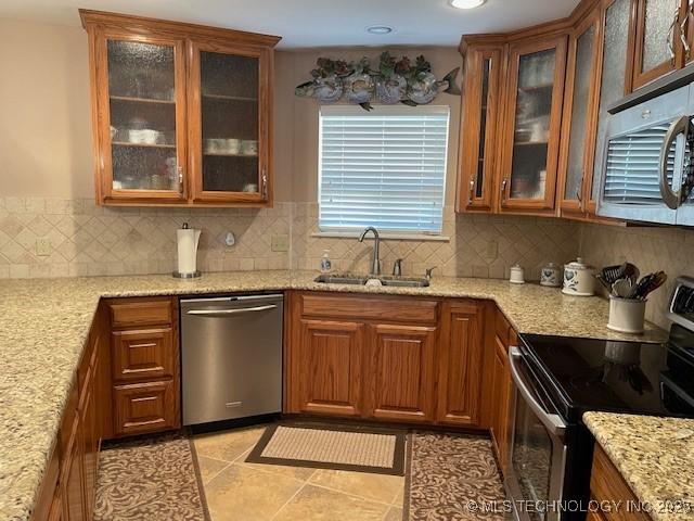 kitchen featuring light stone countertops, brown cabinetry, a sink, appliances with stainless steel finishes, and tasteful backsplash