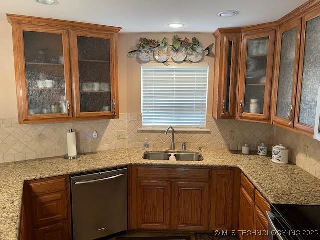 kitchen with light stone countertops, dishwasher, decorative backsplash, brown cabinetry, and a sink